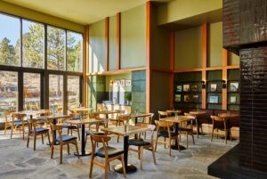 wooden chairs and tables in front of floor to ceiling windows in restaurant with views over mountains