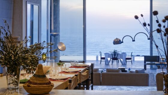 view out of villa with profile of mid century italien lamp in front of pool and dining table looking across to the sea view at La Fiermontina Ocean Morocco