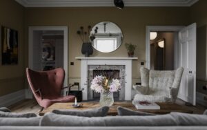 sage green walls, mid century modern pink and cream chairs in front of a traditional fireplace