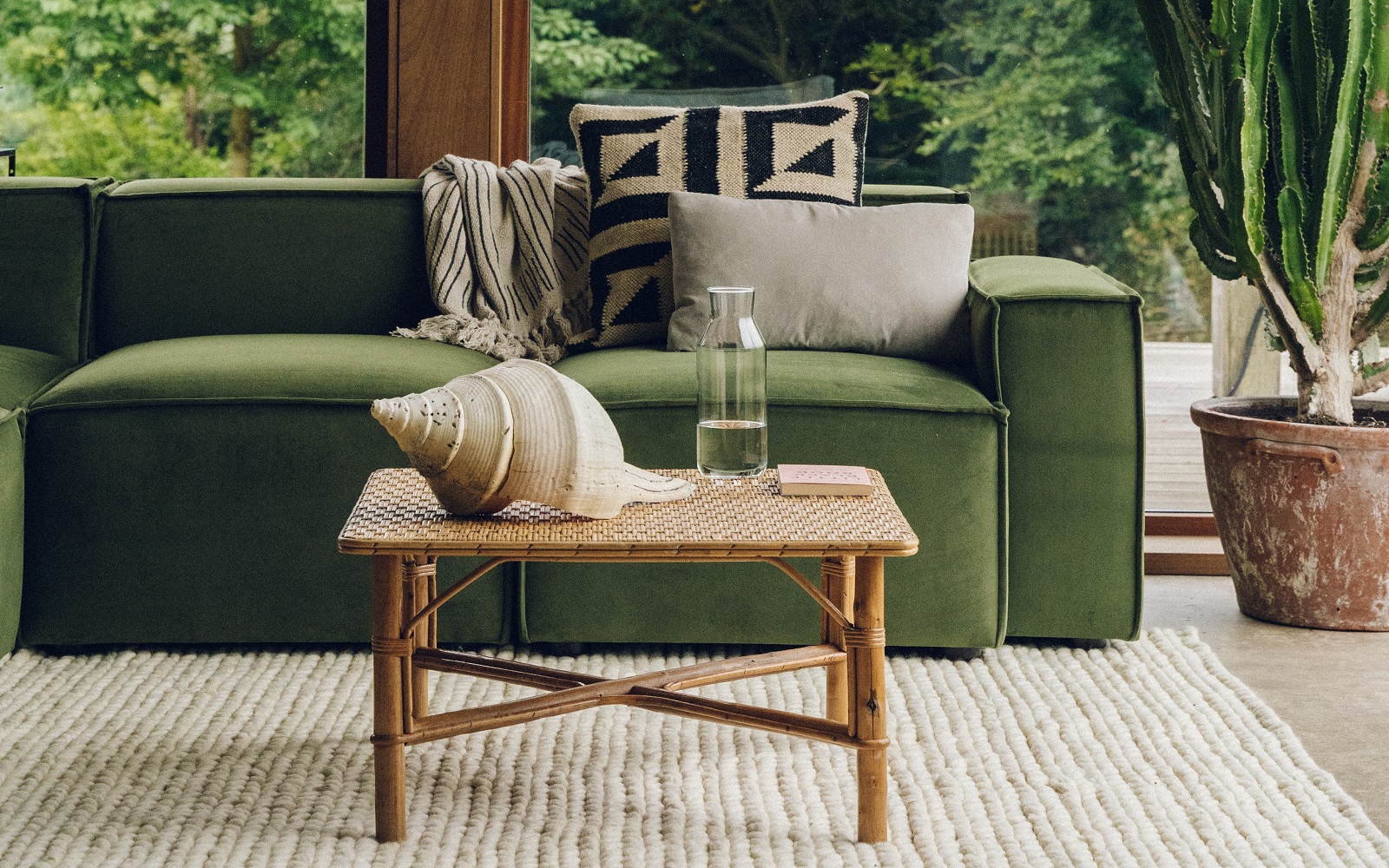 moss green couch with plants in the background and textured natural carpet on the floor