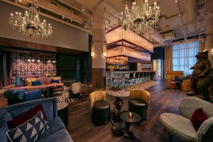 maiximalist hotel lobby with seating in foreground, giant bear statue, chandeliers and bar