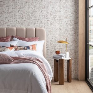 bedroom with soft beige upholstered headboard and tonal textiles thrown on the bed with patterned wallpaper behind