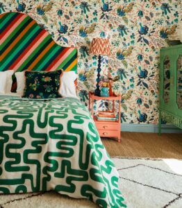 bright striped headboard against botanical print wallpaper and a bold green pattern throw on the bed