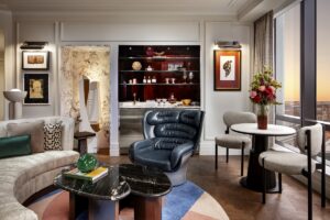 blue leather chair and cream curved couch in front of floor to ceiling glass windows with city view in Raffles Boston suite