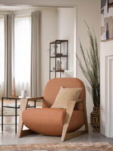 armchair with modern wooden frame covered in saffron coloured fabric next to plants and fireplace