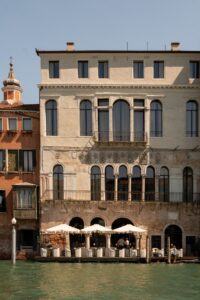 facade of Venice Venice Hotel with umbrellas and seating in front of the canal