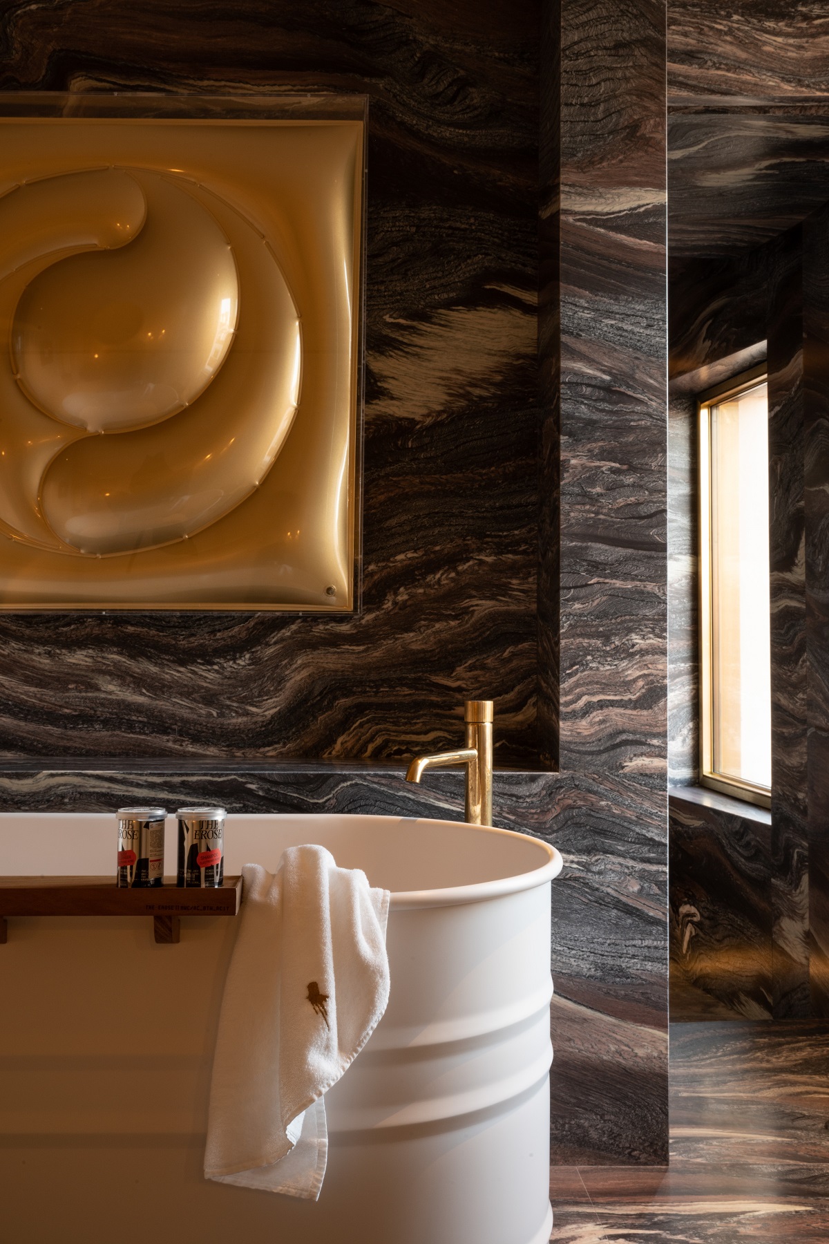 corner of freestanding metal bath with gold artwork above on marble wall