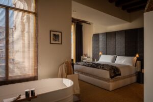 freestanding white metal bath in front of window leading through to guestroom with panelled headboard