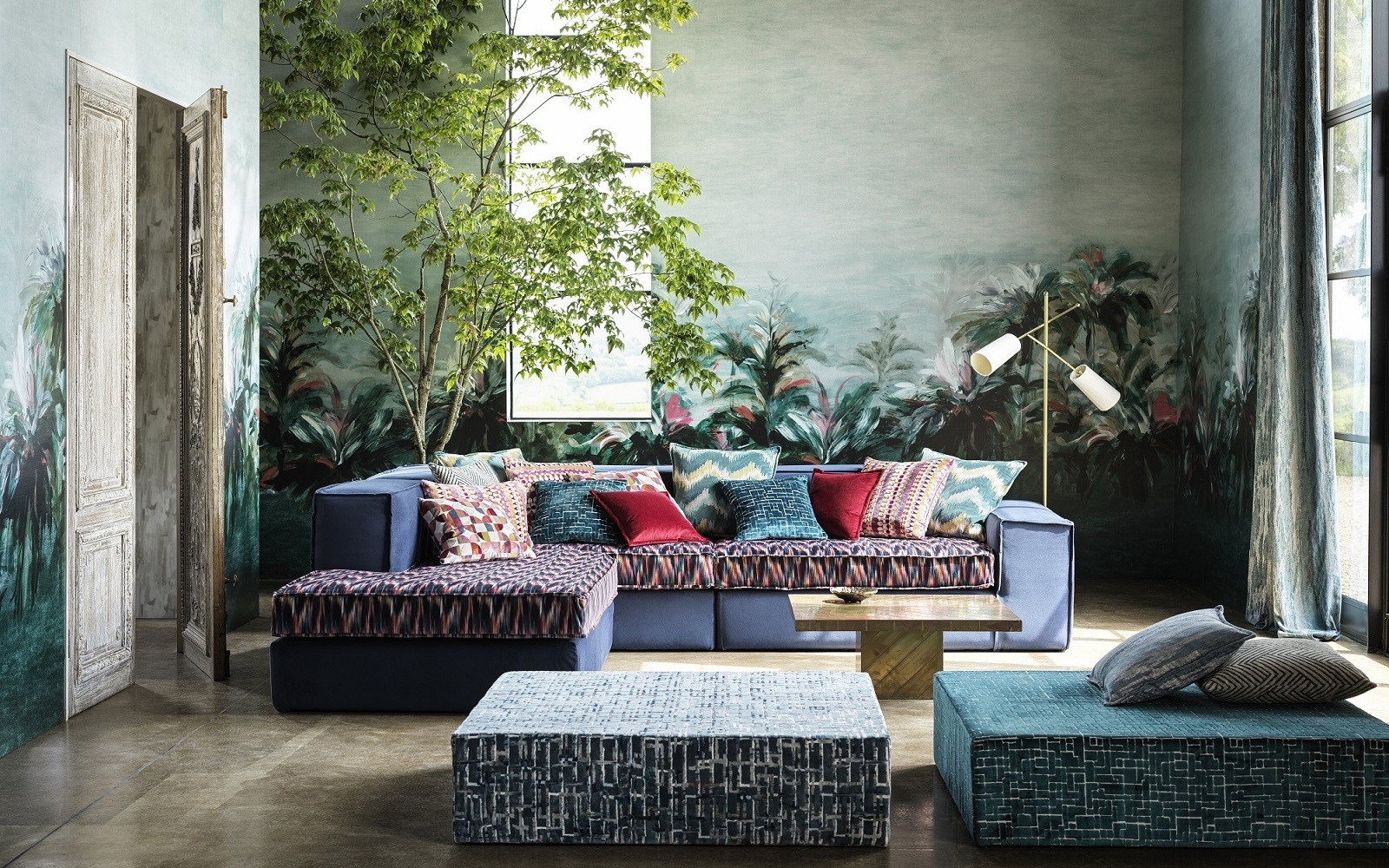 patterned upholstered couch with a pile of contrasting cushions in a room with plants and natural light